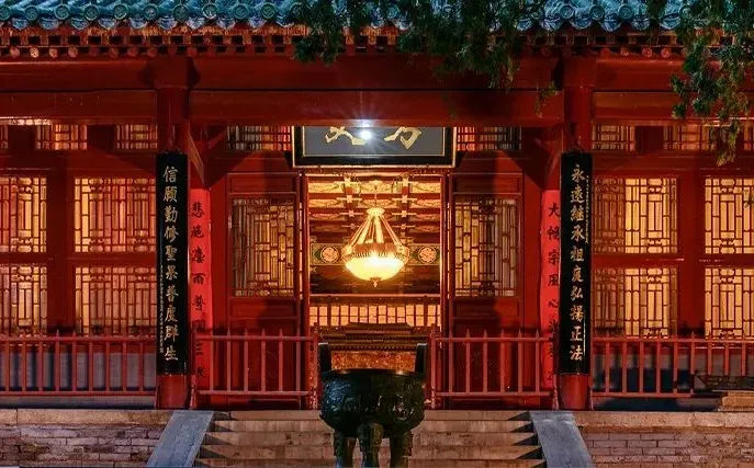 Illuminated Shaolin temple entrance with red columns, incense burner, and traditional lattice windows