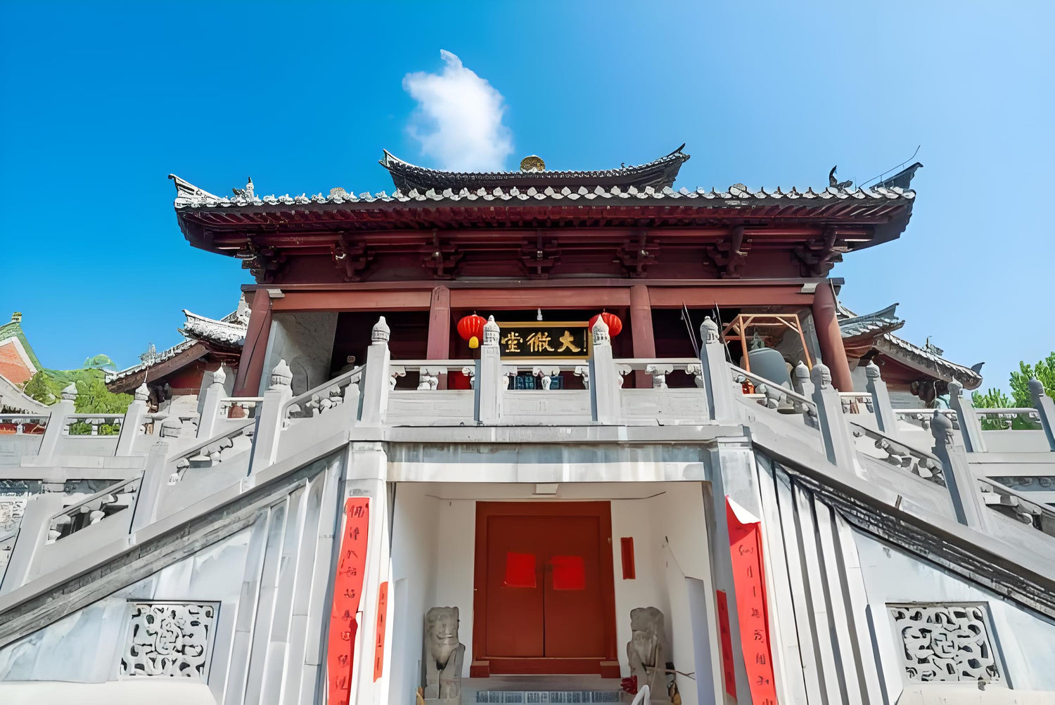 Traditional Chinese temple with red lanterns, stone lions, and ornate architecture under blue sky