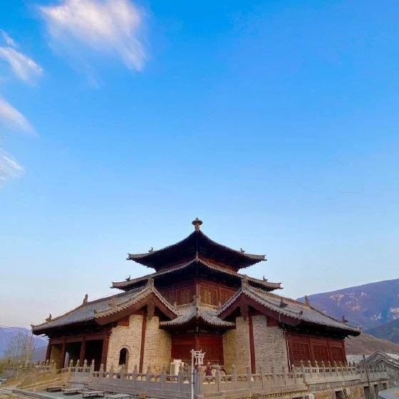 Traditional Chinese Buddhist temple with ornate tiled roof under blue sky and mountain backdrop