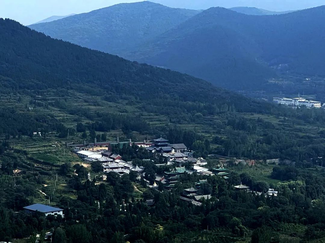 Aerial view of a Buddhist temple complex surrounded by lush green mountains and forest.