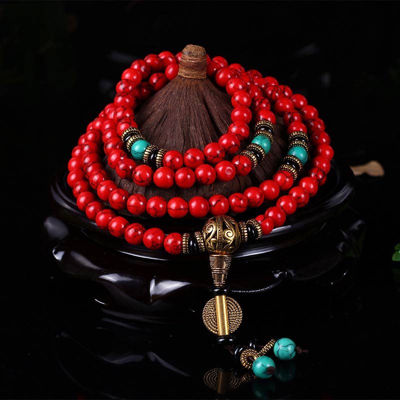 Red and turquoise Buddhist prayer beads with gold accents, displayed on dark stand for meditation and mindfulness