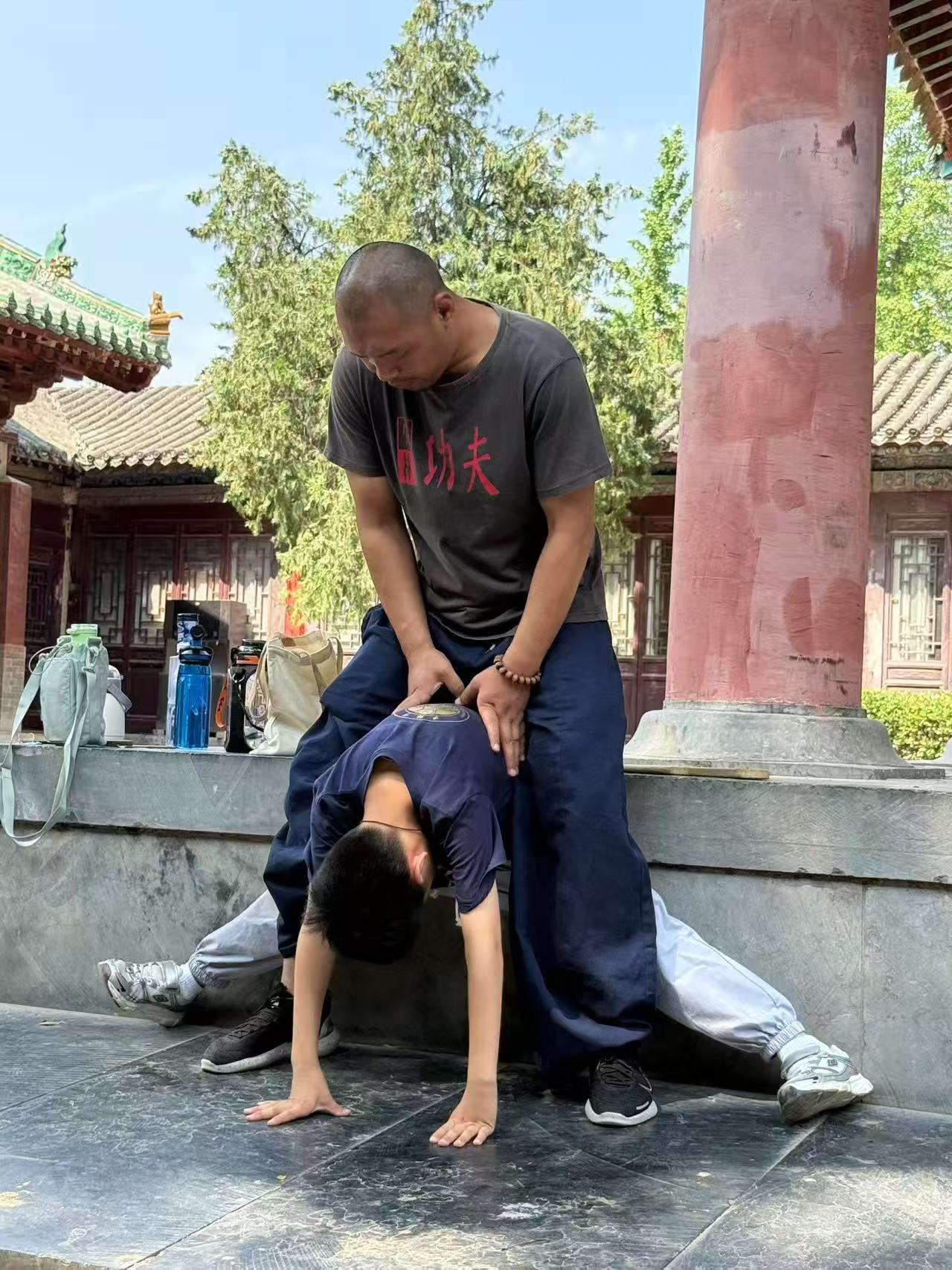 Shaolin kung fu instructor helping student stretch outdoors at traditional temple courtyard