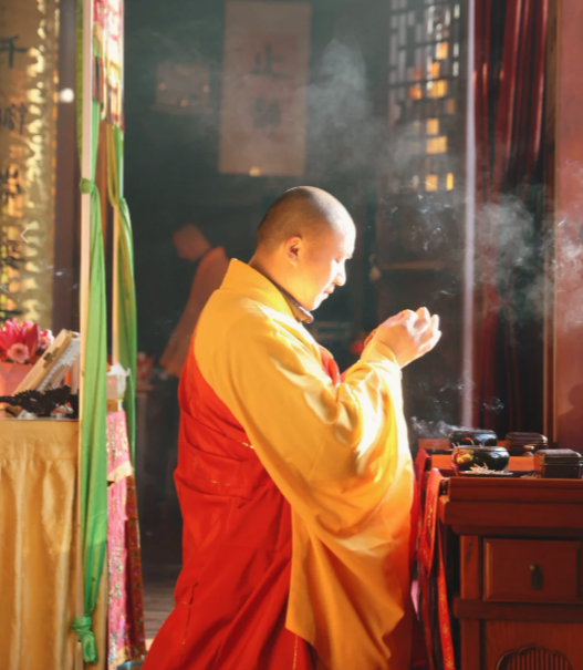 Monk in yellow and red robes praying with incense smoke in a serene Buddhist temple setting