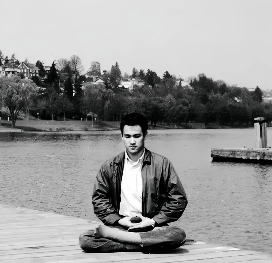 Man meditating in lotus pose on wooden dock by lake, practicing mindfulness and peace