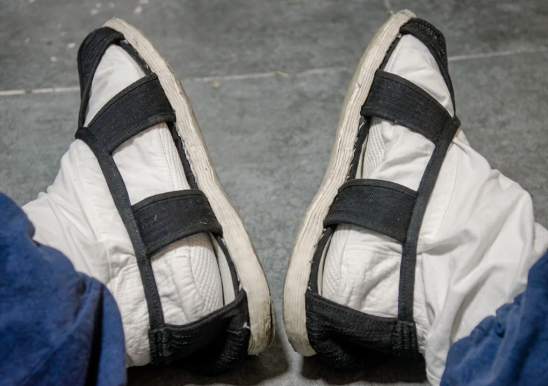 White martial arts sandals with black straps, worn with blue robe for Shaolin-inspired practice and mindfulness.
