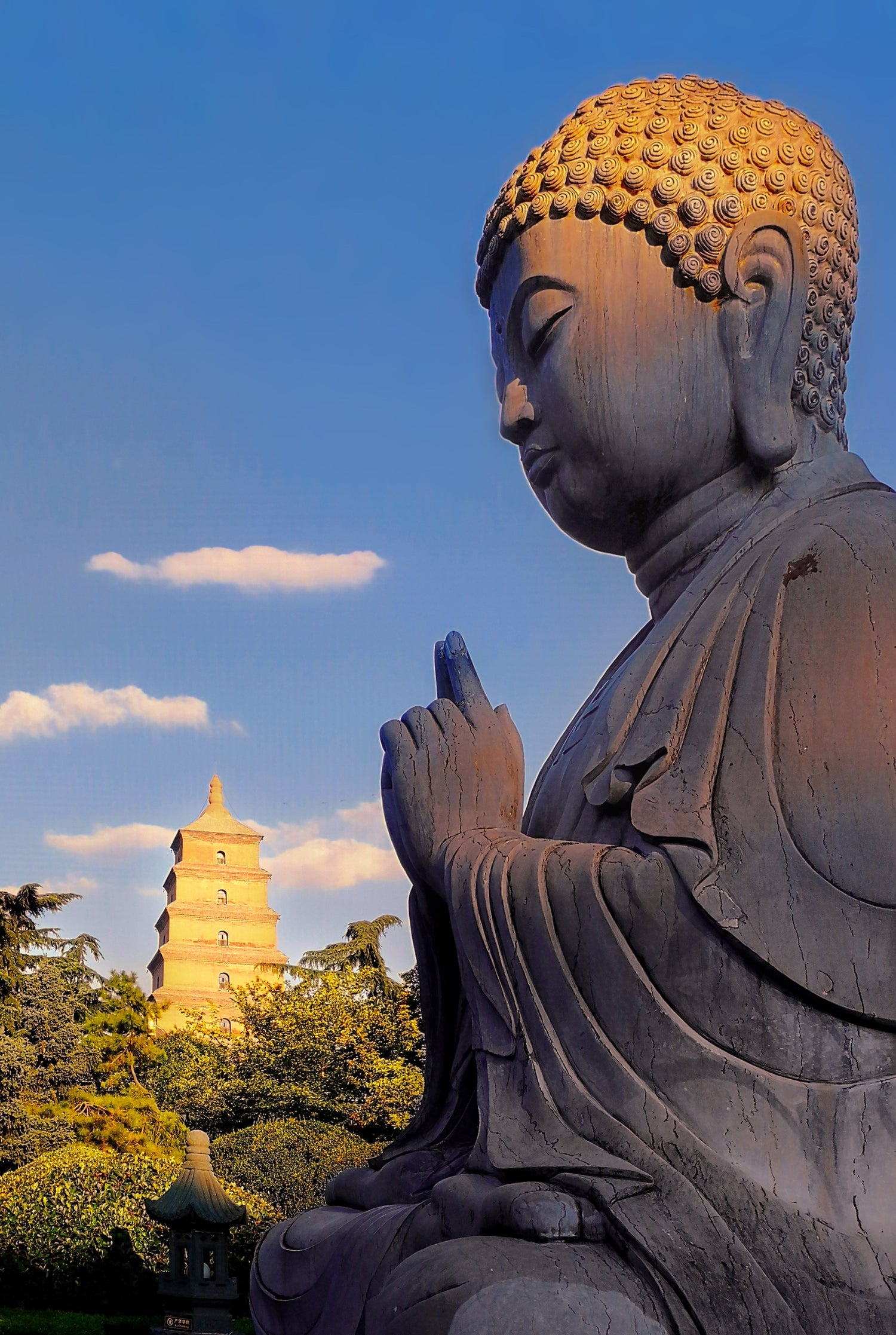 Shaolin-inspired Buddha statue in meditative pose outdoors with a pagoda and blue sky