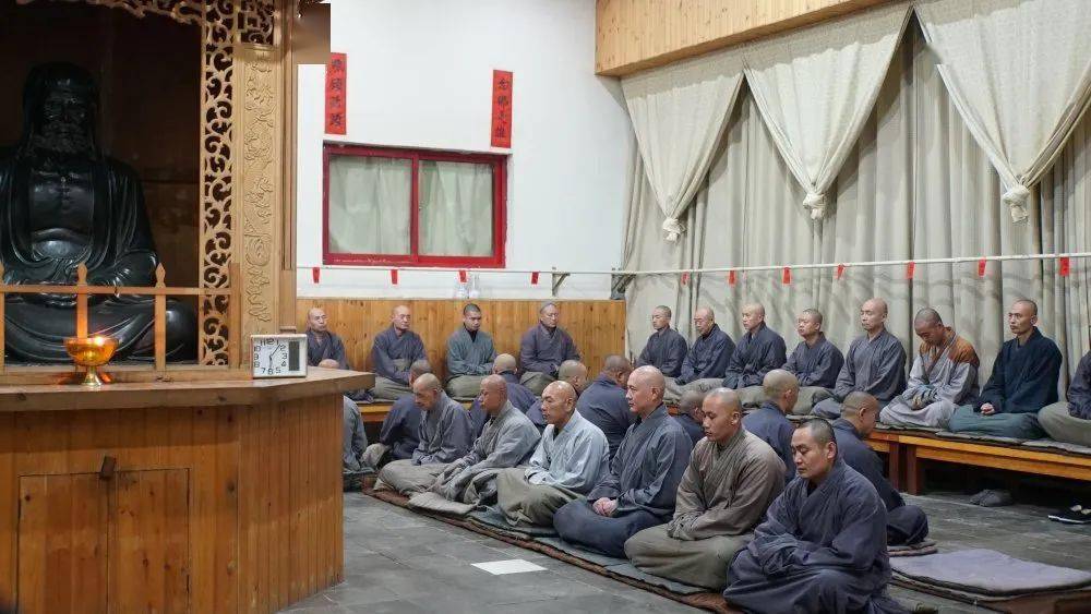 Shaolin monks meditating in a temple hall beside a large Buddhist statue and altar.
