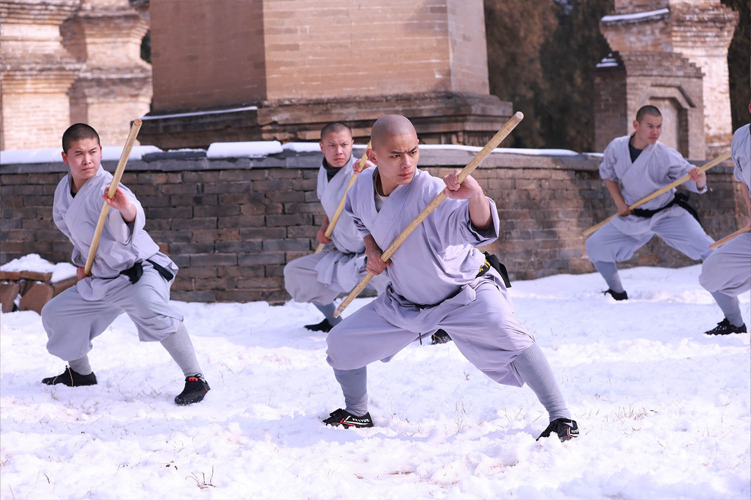 Shaolin monks practicing kung fu with staffs in snow by ancient brick pagodas