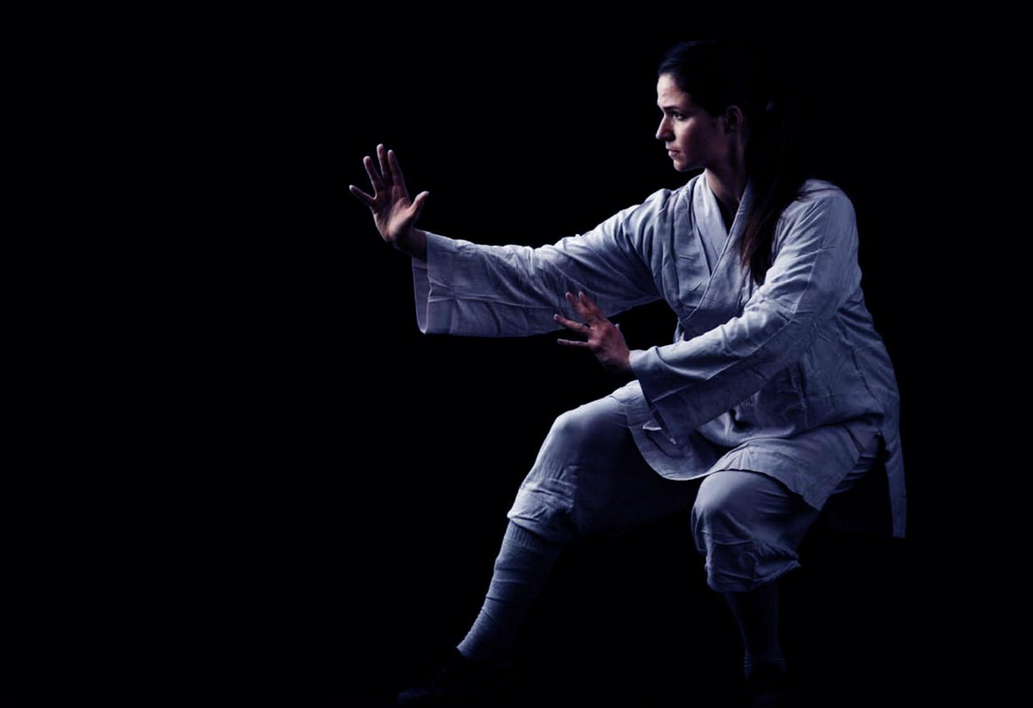Woman in martial arts pose wearing traditional Shaolin kung fu uniform on dark background