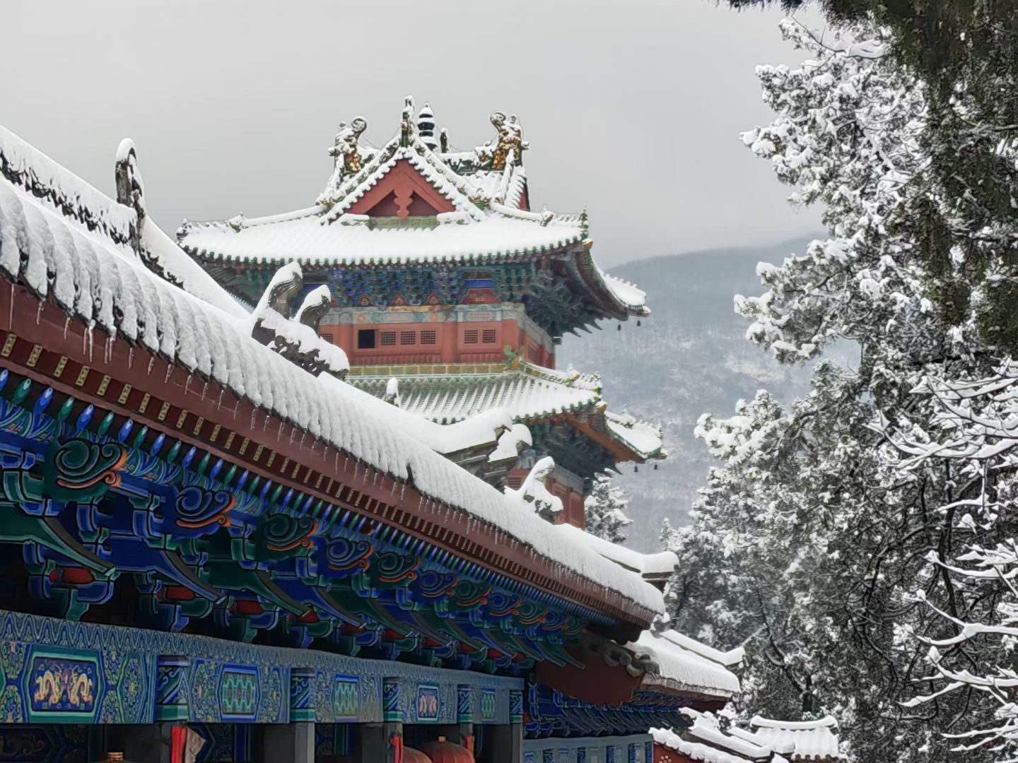Traditional Chinese temple with snow-covered roofs and ornate details in a winter landscape
