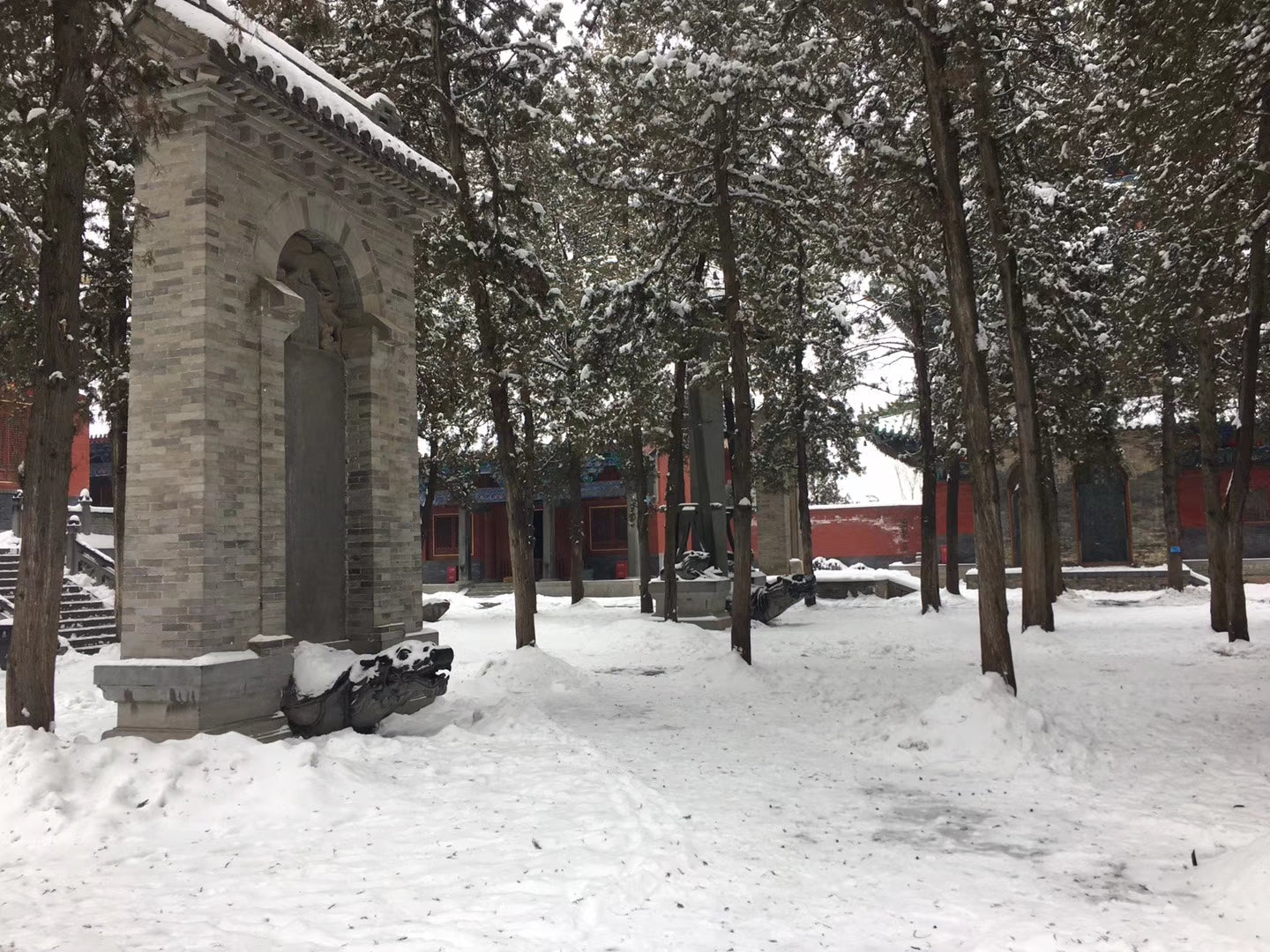 Shaolin temple courtyard in winter, stone archway and pine trees covered in snow