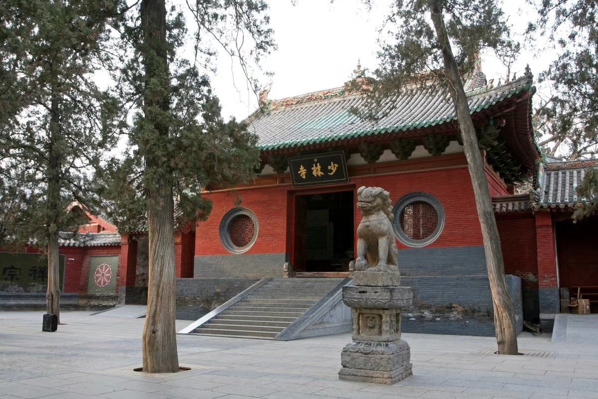 Shaolin Temple entrance with traditional Chinese architecture, stone lion statue, and green trees