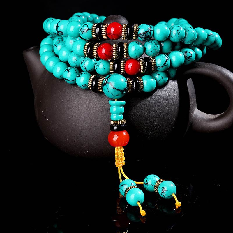 Turquoise prayer beads with red and black accents, displayed on a dark ceramic teapot for mindful meditation and Buddhist altar decor.