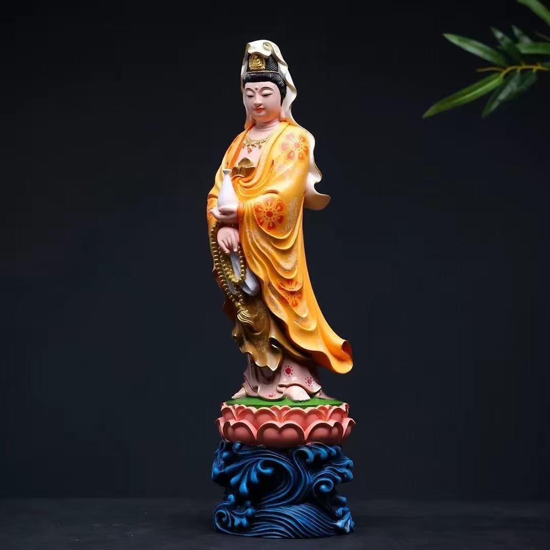 Guan Yin statue in golden robe holding vase, standing on lotus base with wave design, Buddhist altar decor
