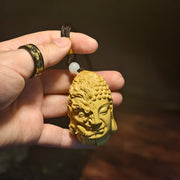 Hand holding carved Buddha and demon face pendant with prayer bead, Buddhist spiritual jewelry