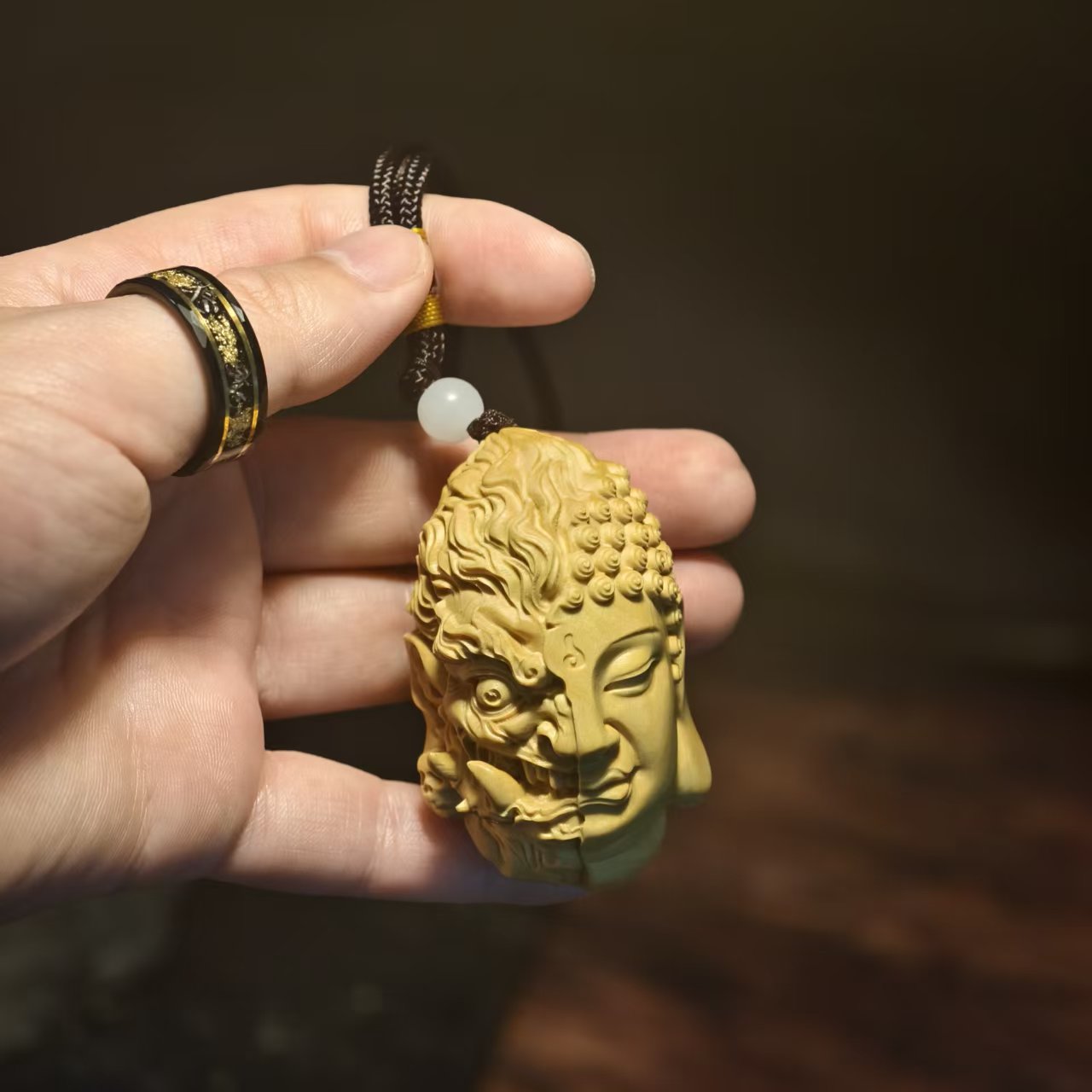 Hand holding carved Buddha and demon face pendant with prayer bead, Buddhist spiritual jewelry
