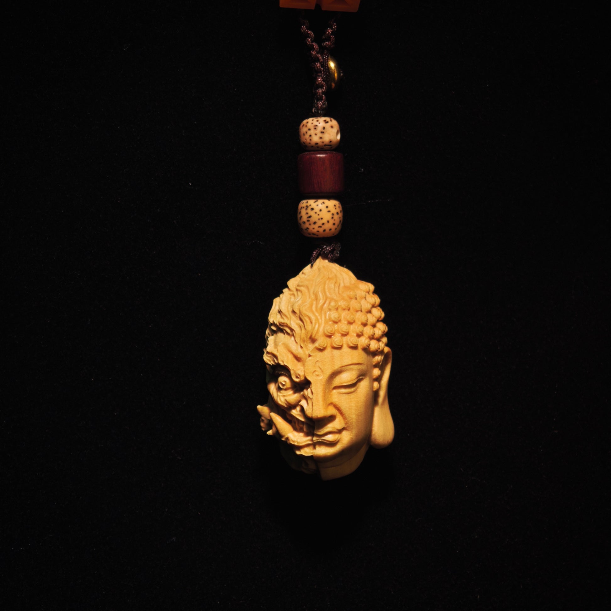 Hand-carved wooden Buddha head pendant with dual serene and fierce faces, prayer beads, and spiritual decor.