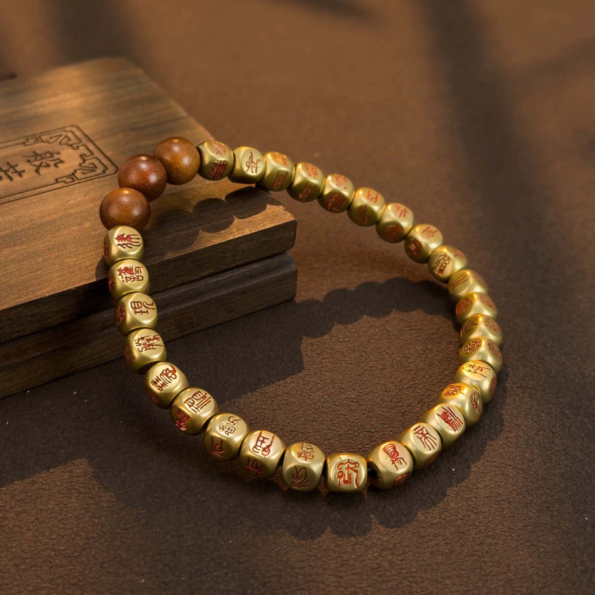 Golden prayer beads with red inscriptions, resting on wooden box, ideal for mindfulness and meditation