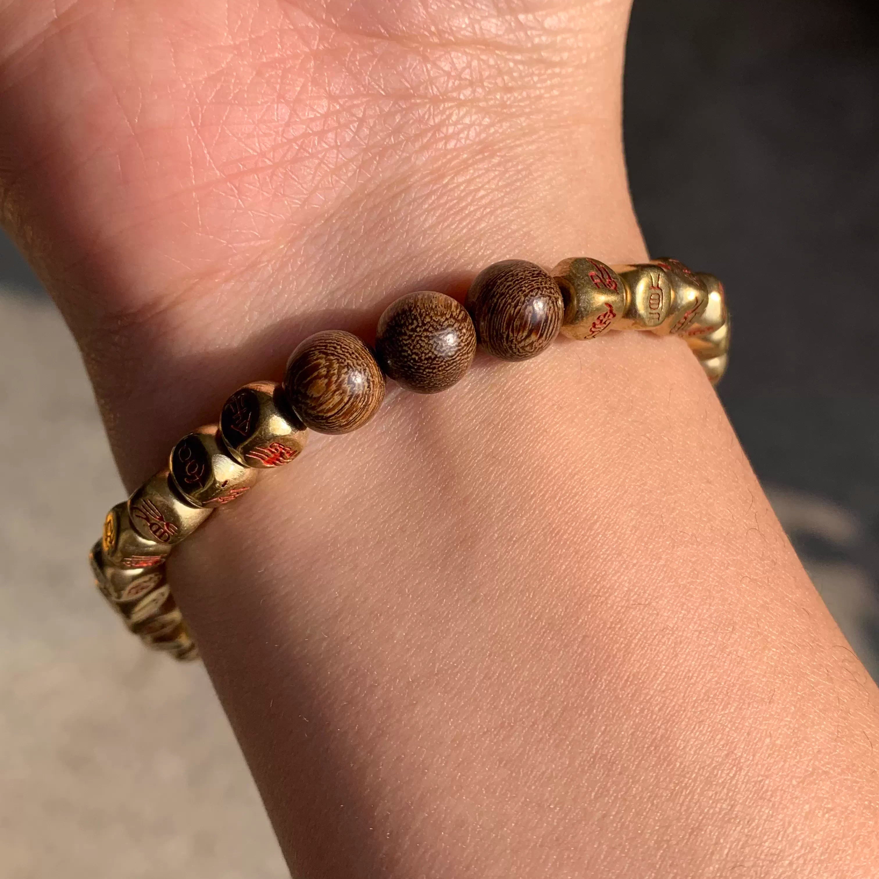 Wooden and gold prayer beads bracelet with engraved symbols on wrist
