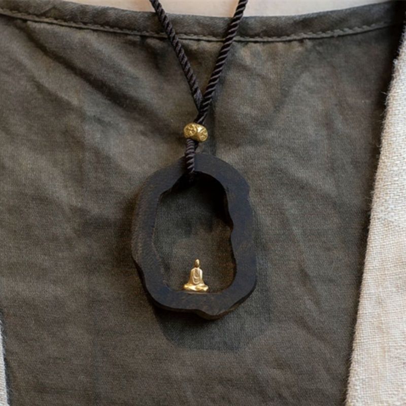 Wooden pendant with gold Buddha statue, worn on dark cord necklace for mindful style